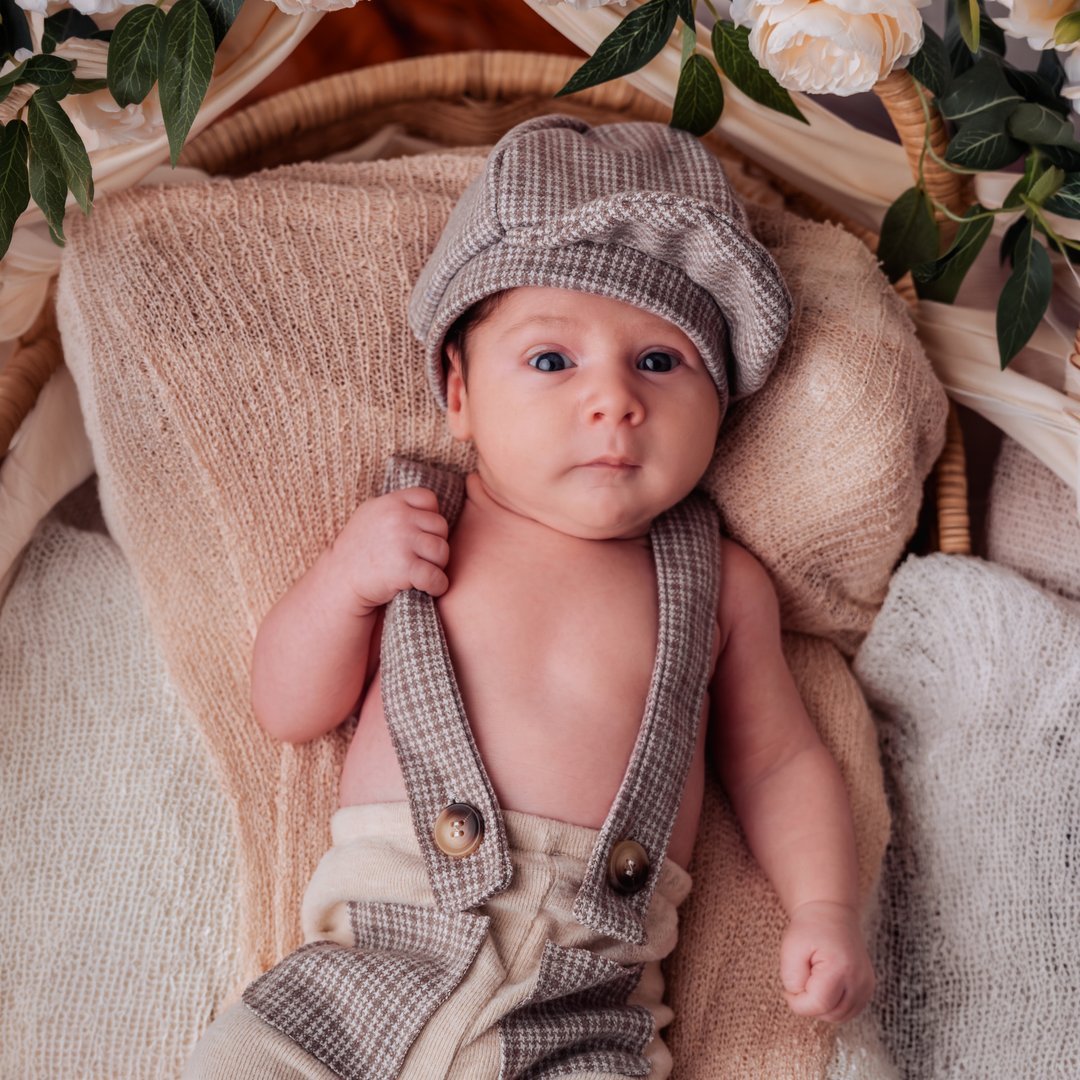 Un bebé con gorro de punto recostado en una cesta acolchada.