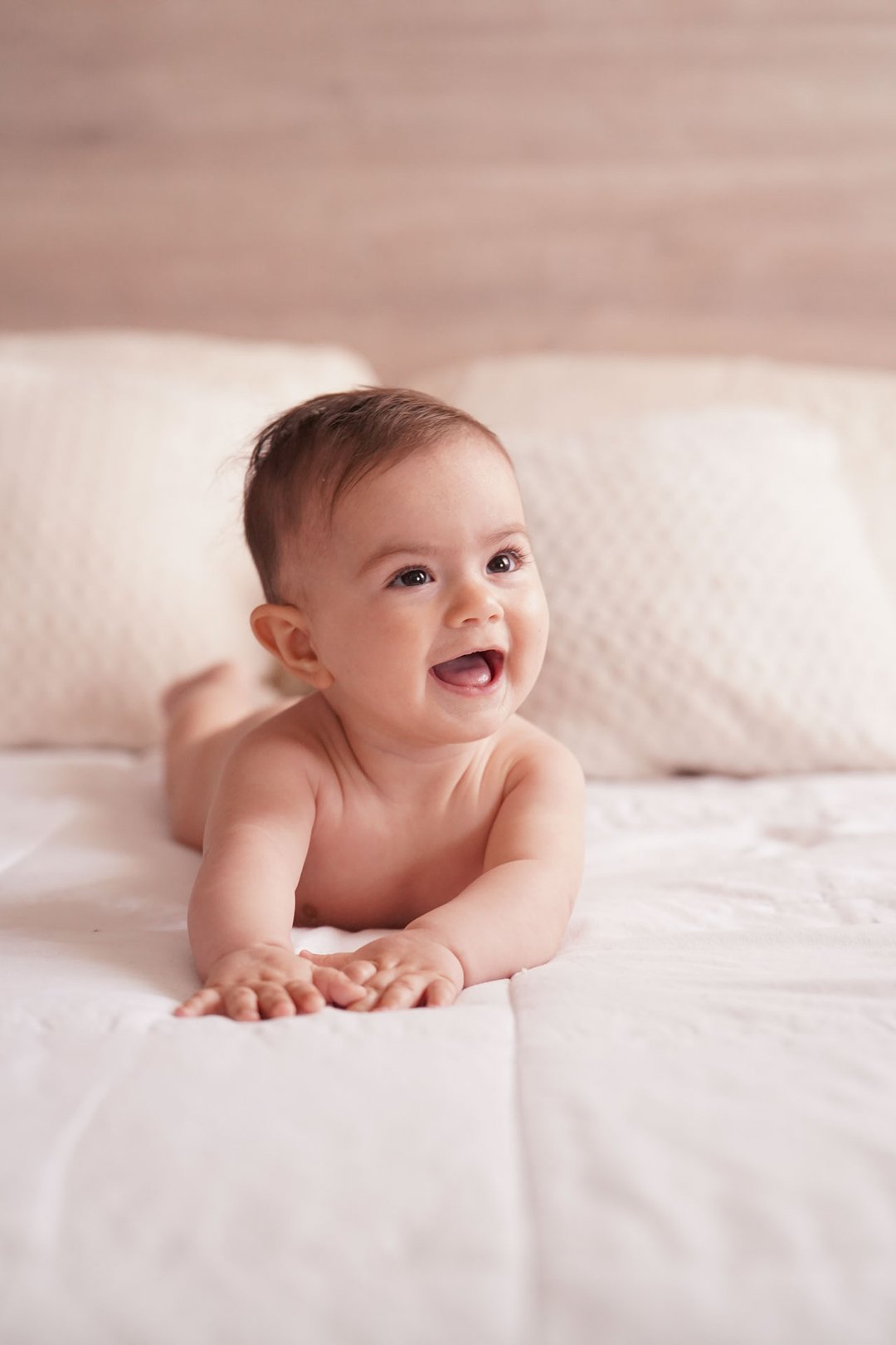 Un bebé sonriente tumbado boca abajo sobre una manta clara.