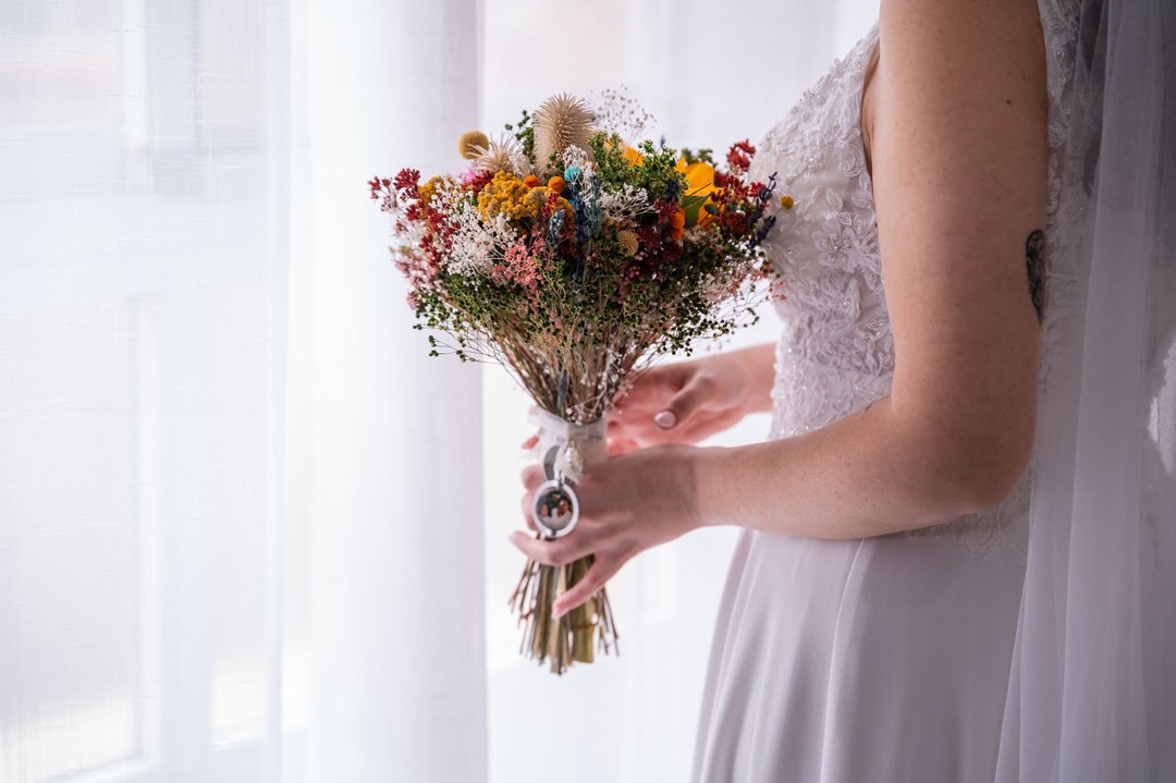 Detalle del ramo de flores de Rosi y su vestido de novia junto a una ventana.
