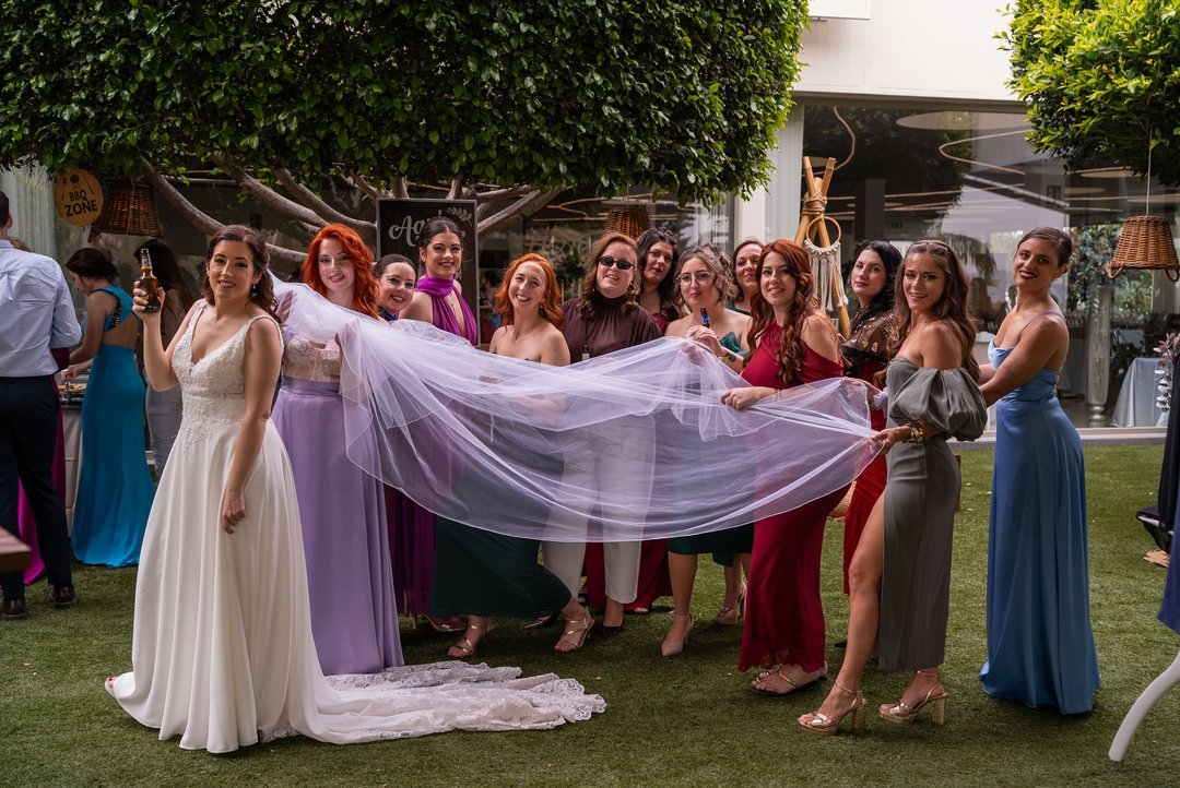 Rosi y un grupo de invitadas sostienen el velo de novia en el jardín.