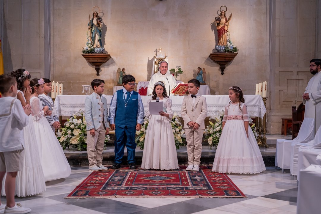 Niña leyendo junto a otros niños de comunión ante el altar de la iglesia