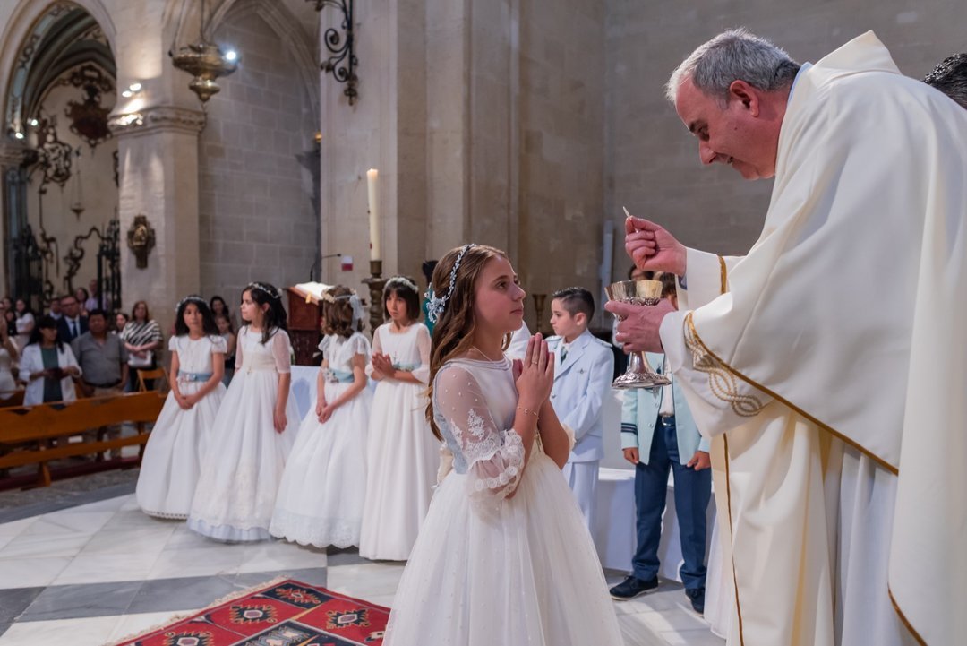 Niña con las manos juntas ante el sacerdote en su primera comunión