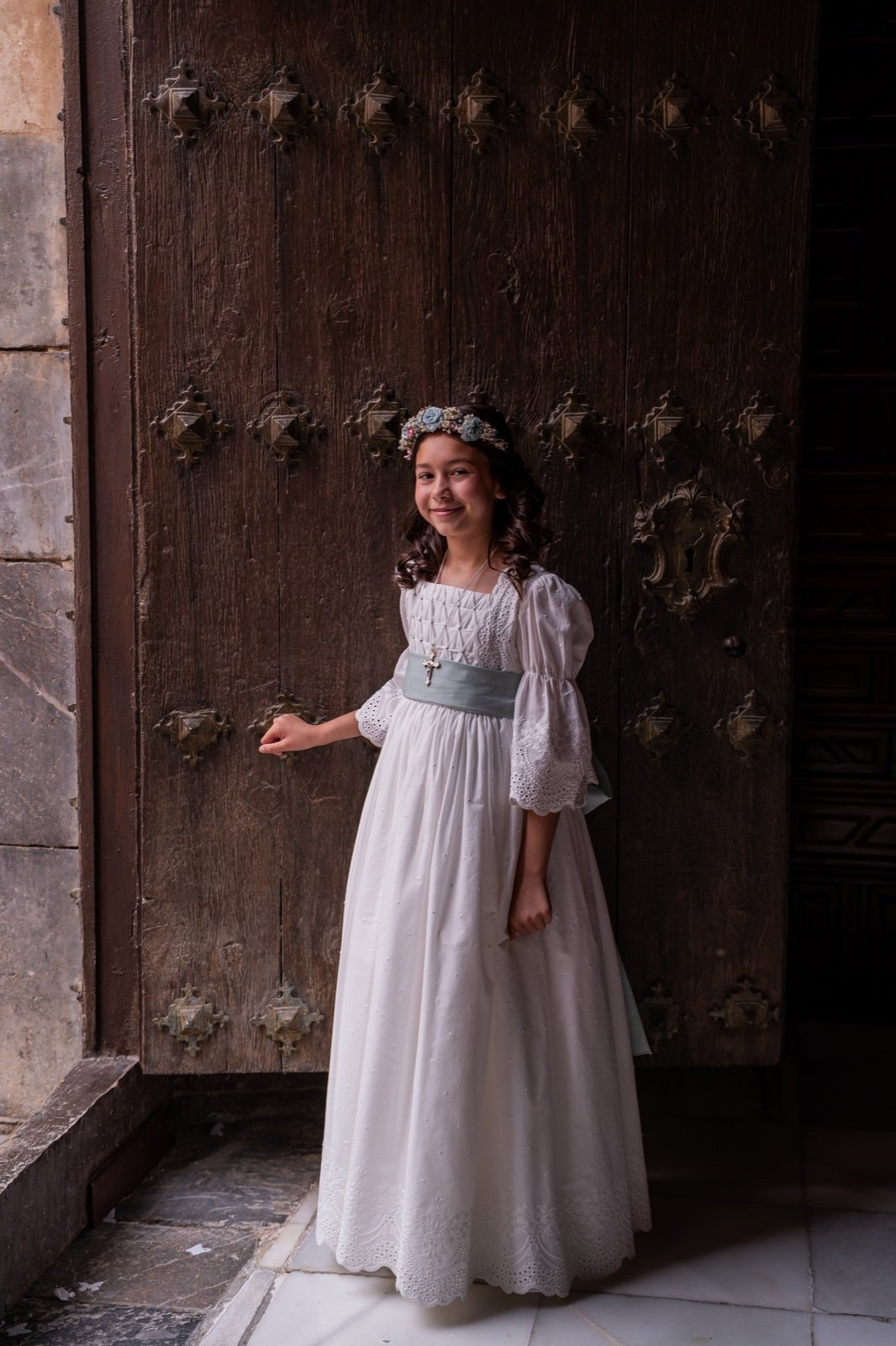 Niña con vestido de comunión y fajín verde junto a la puerta de la iglesia