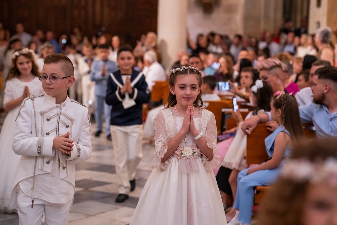 Niños de comunión de pie en el pasillo de la iglesia junto a sus familias