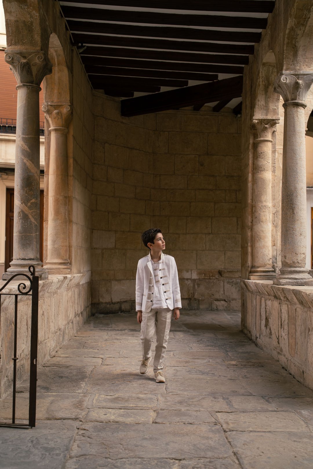 Un niño con traje de comunión en un corredor con columnas de piedra.
