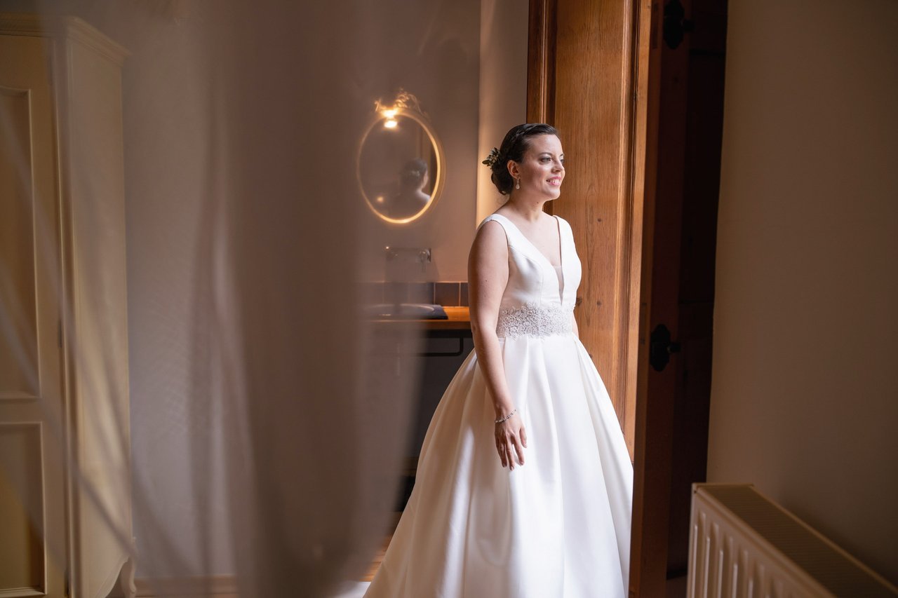 Una novia con vestido blanco junto a una ventana.