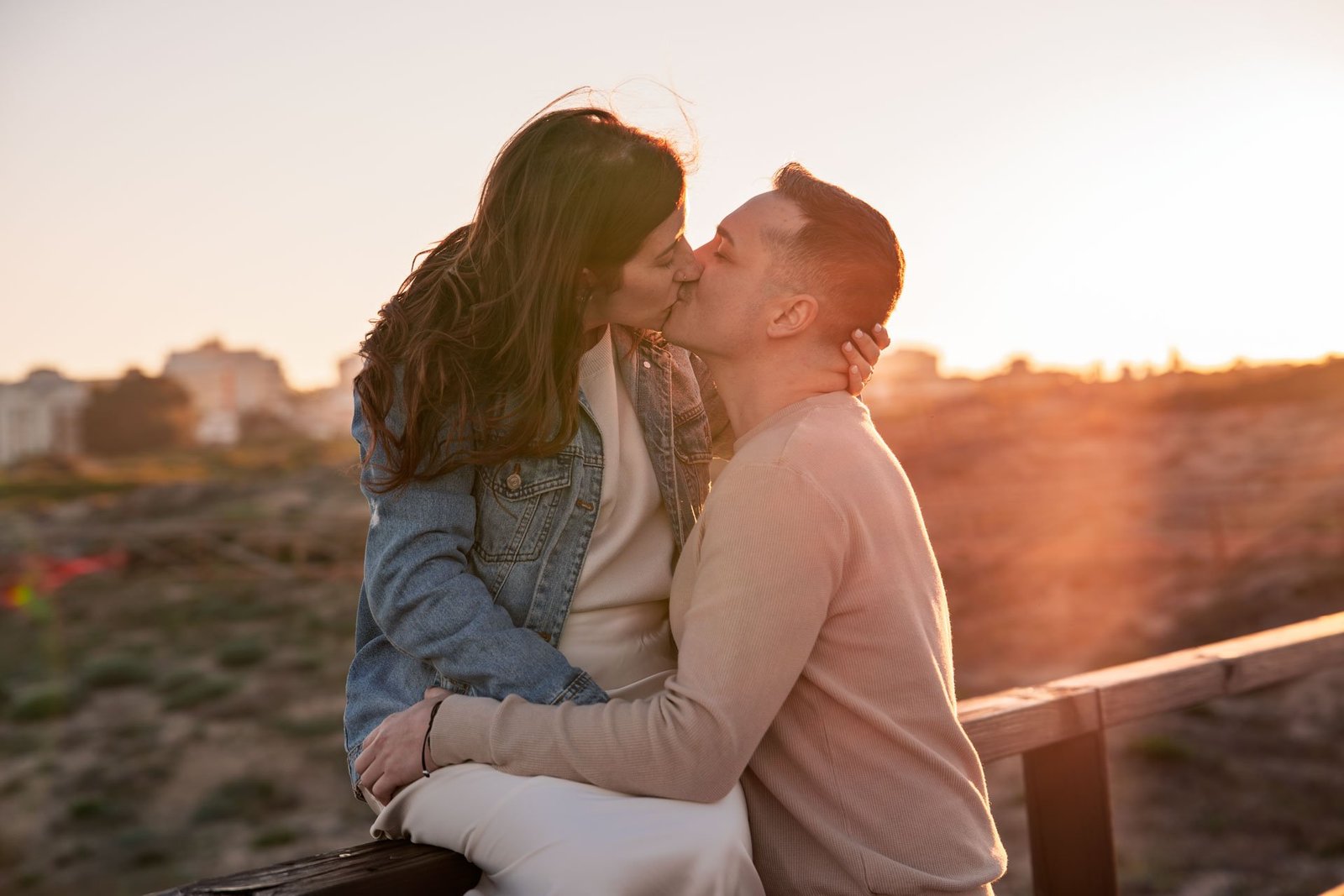 Una pareja se besa junto a una barandilla al atardecer.
