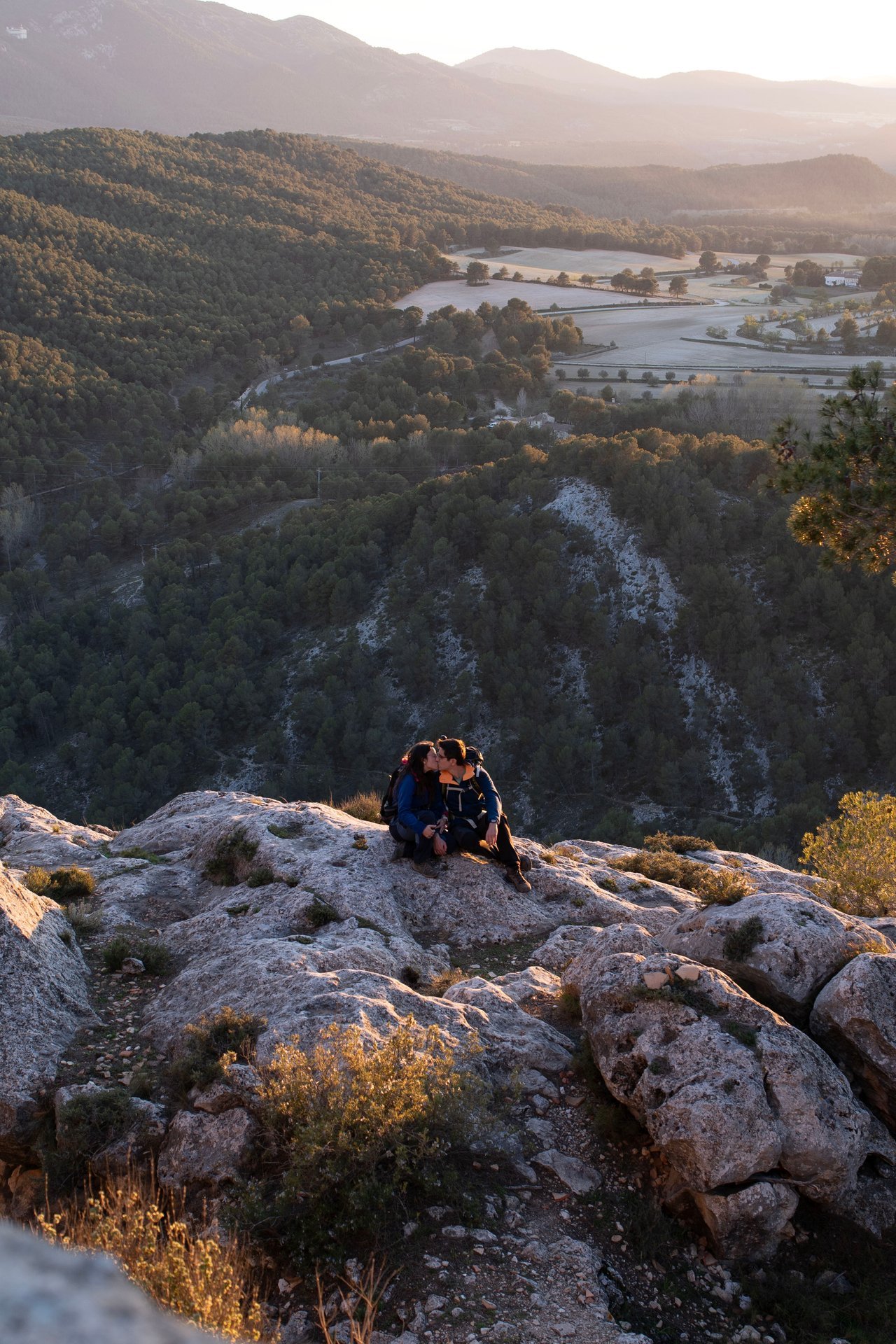 Una pareja sentada sobre unas rocas frente a un paisaje de montañas.