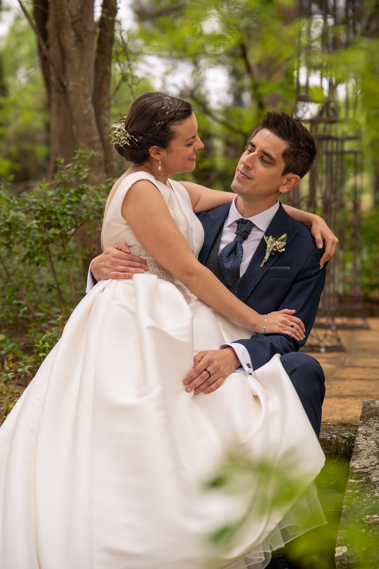 Ana y David abrazados durante su reportaje de boda en un jardín.
