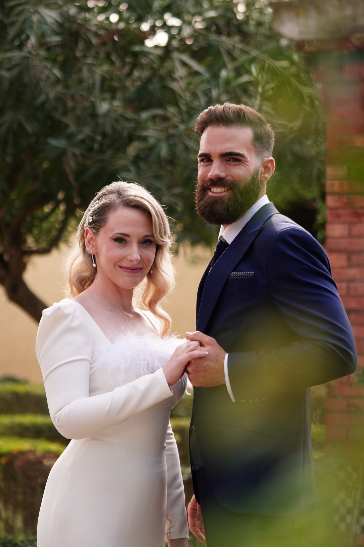 Marta y Alejandro cogidos de las manos durante su reportaje de boda en un jardín.