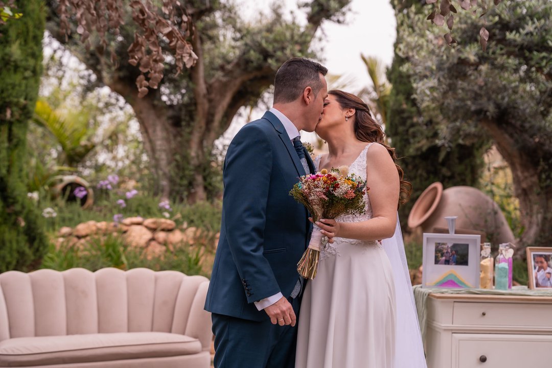 Paco y Rosi se besan tras la ceremonia con el ramo de novia entre sus manos.