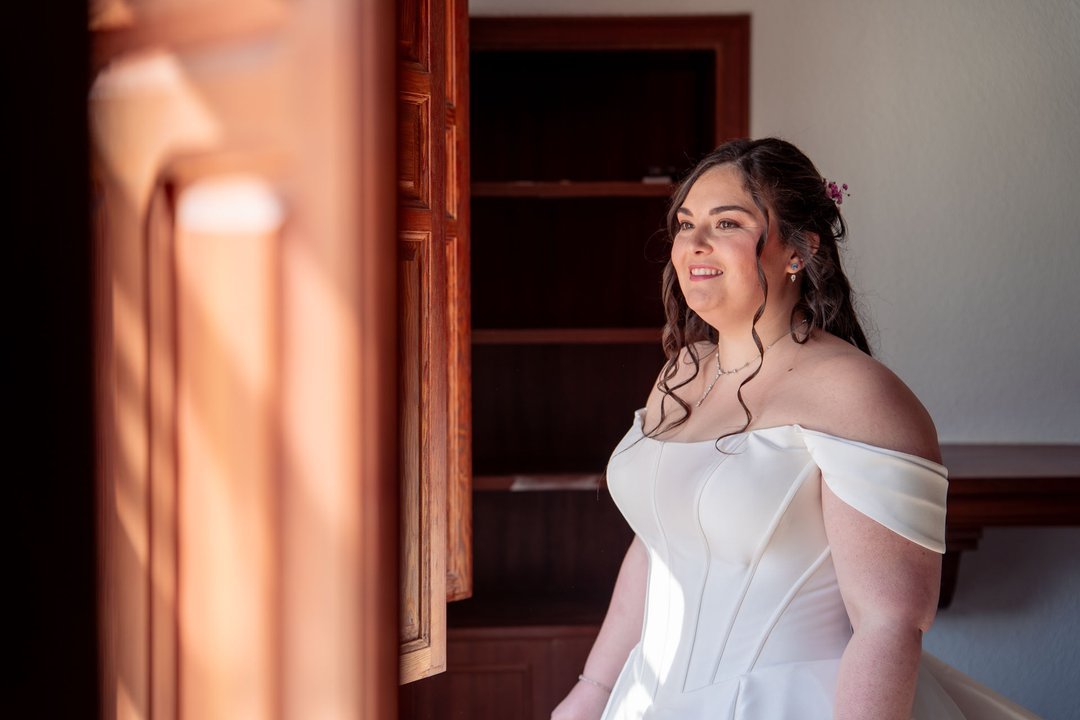 Tamara con su vestido de novia junto a una ventana de madera.