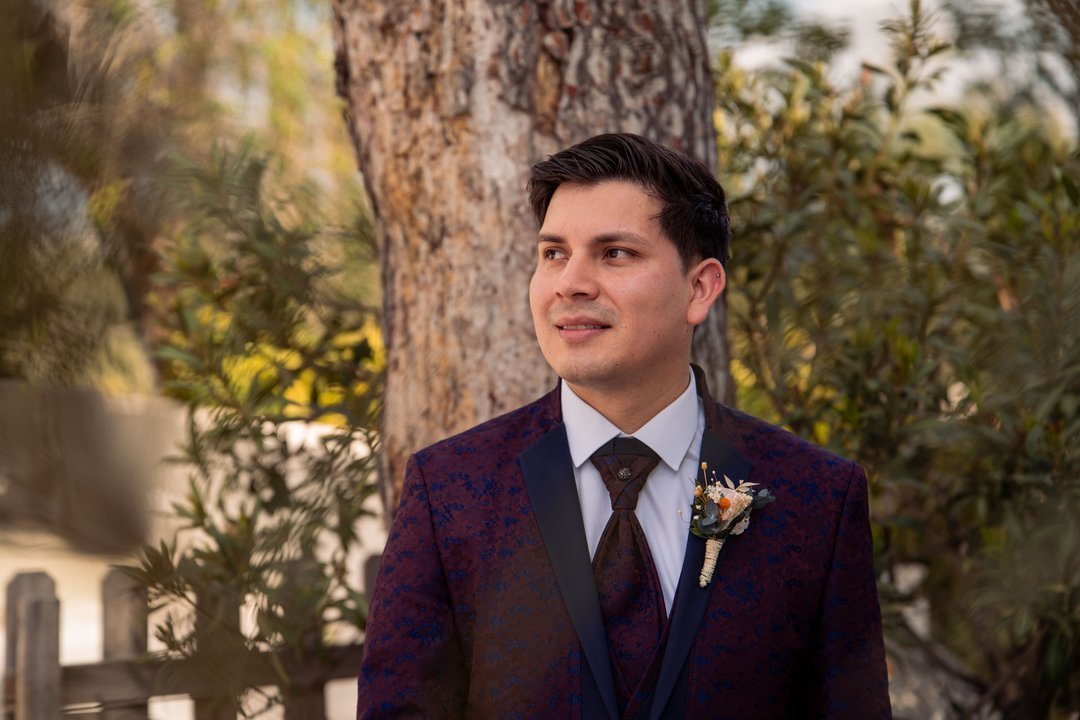 Stoni con traje de novio junto a un árbol durante su reportaje de boda.