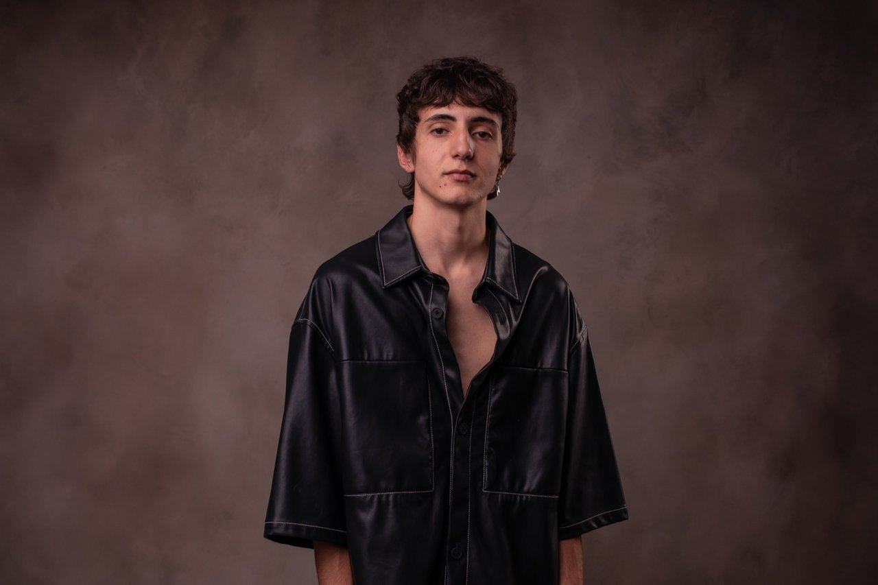 Retrato en estudio de un joven con camisa negra sobre fondo marrón