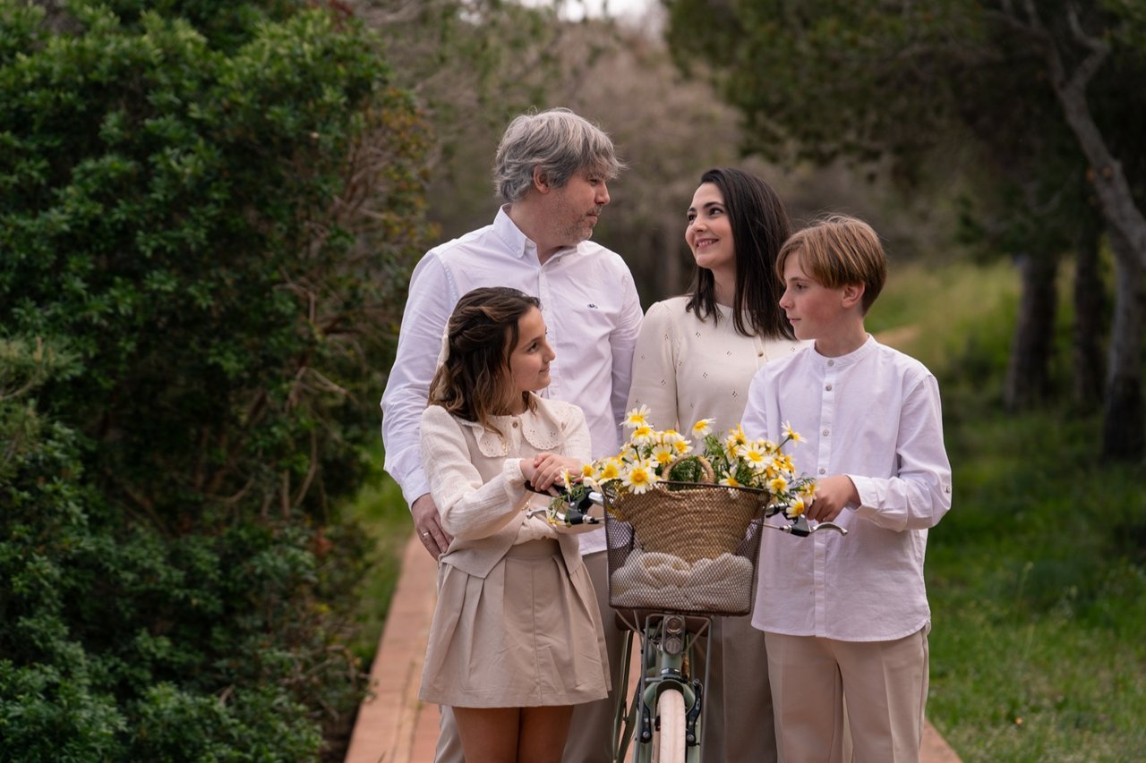 Familia con dos hijos junto a una bicicleta con una cesta de flores en un entorno natural