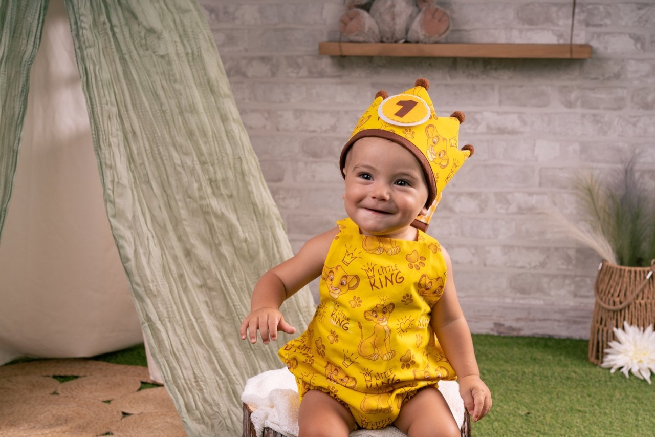 Bebé sonriendo con un conjunto amarillo y una corona de primer cumpleaños en el estudio